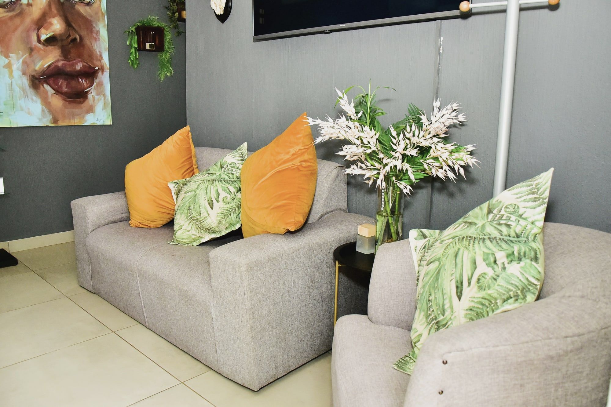 The waiting lounge: grey sofas with mustard and leaf-print cushions under a painted portrait.